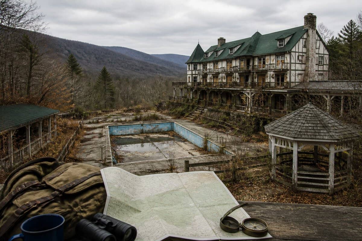 An abandoned resort complex sits among wooded Pocono Mountains beside an unmarked map and compass.