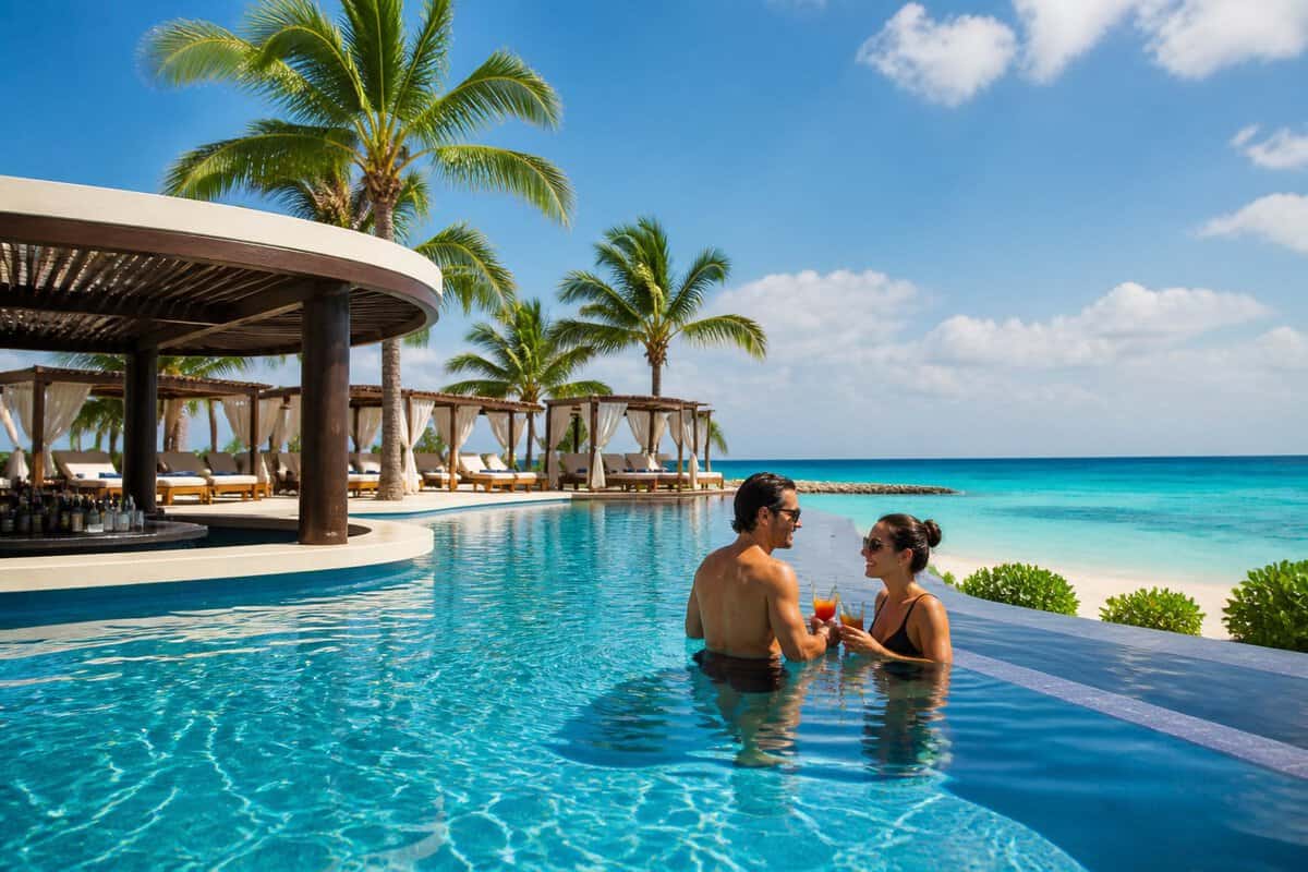 An adult couple relaxes beside an infinity pool at a tropical Cancun beachfront resort.