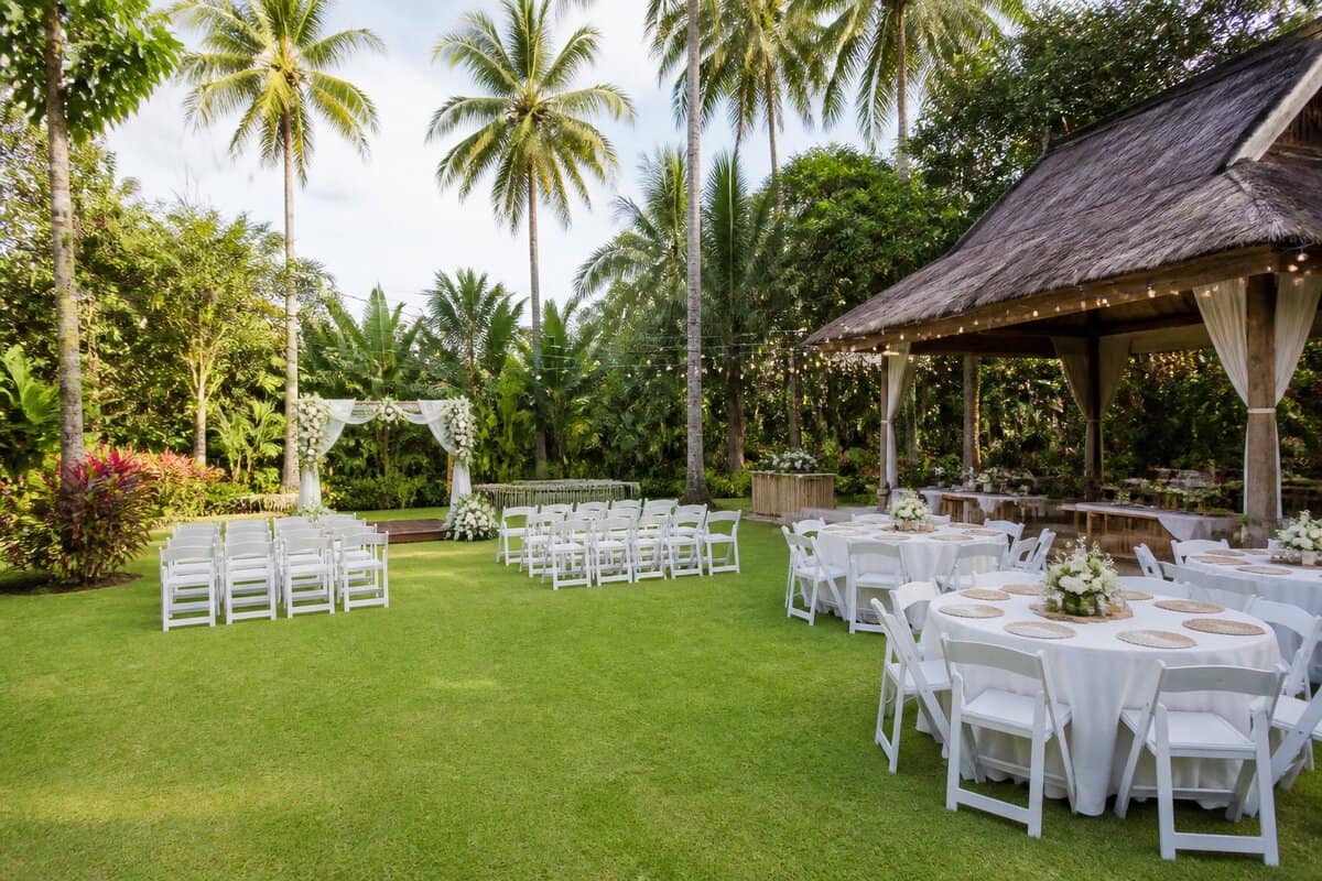 A simple tropical garden wedding venue in the Philippines with white chairs, a floral arch, and modest reception tables.