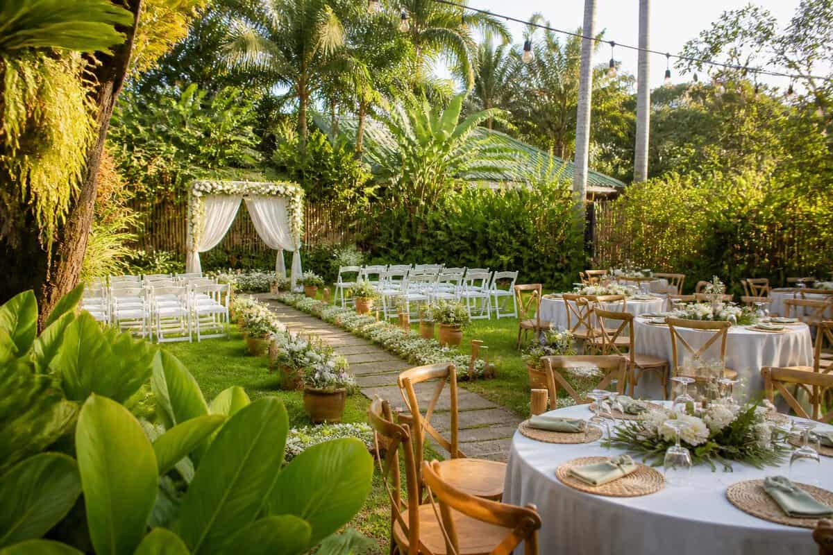 A tropical garden wedding venue with a floral ceremony arch, white chairs, and simple reception tables.