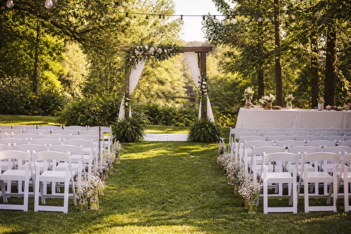A simple outdoor wedding ceremony setup in a green park with chairs, a decorated arbor, and a small reception table.