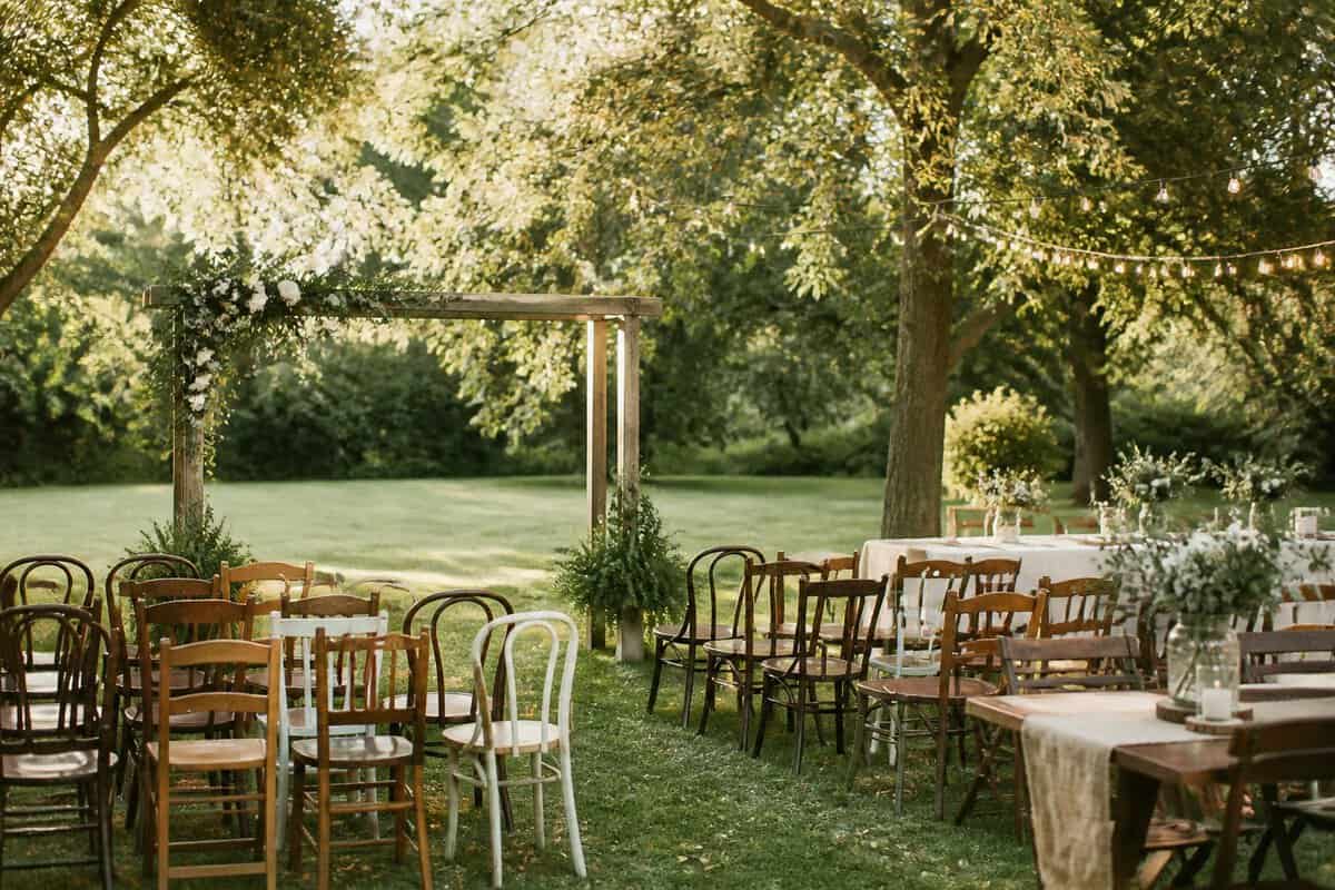 An intimate outdoor wedding ceremony and reception setup in a sunlit garden with simple floral decorations and wooden seating.