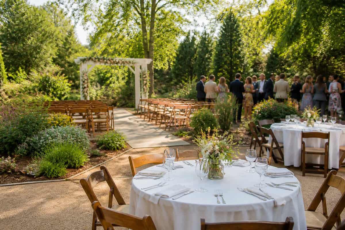 A modest outdoor wedding venue with a flower-decorated arch, neatly arranged chairs, and simple reception tables.