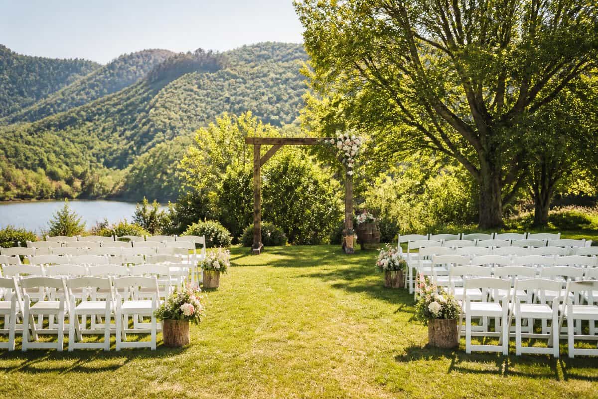 An outdoor wedding ceremony setup with simple chairs, a floral arch, and a scenic natural landscape.