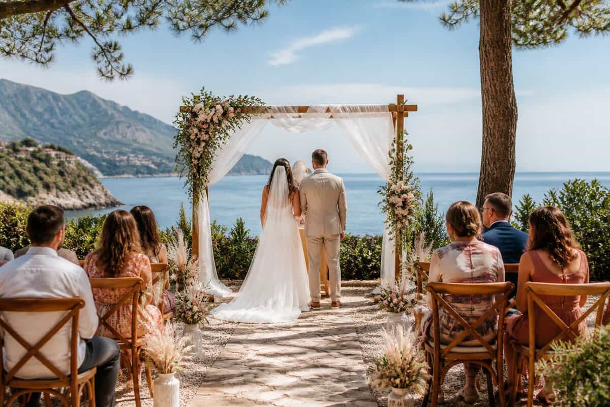 A couple celebrates with guests at a small outdoor wedding venue overlooking the sea.