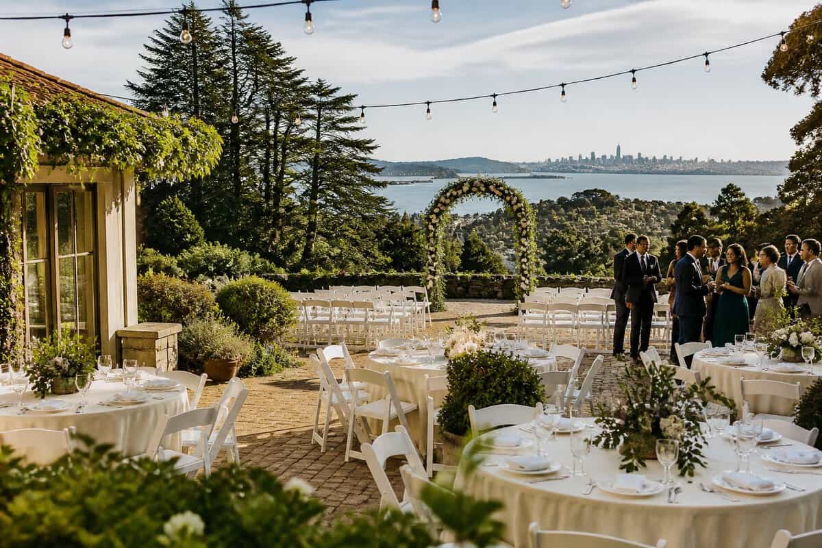 An affordable outdoor wedding venue with simple decorated tables, white ceremony chairs, string lights, and green Bay Area hills in the background.