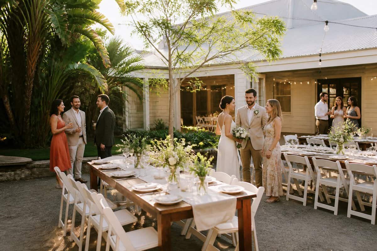 An intimate outdoor wedding reception in a leafy Brisbane venue with simple elegant decorations and guests mingling.