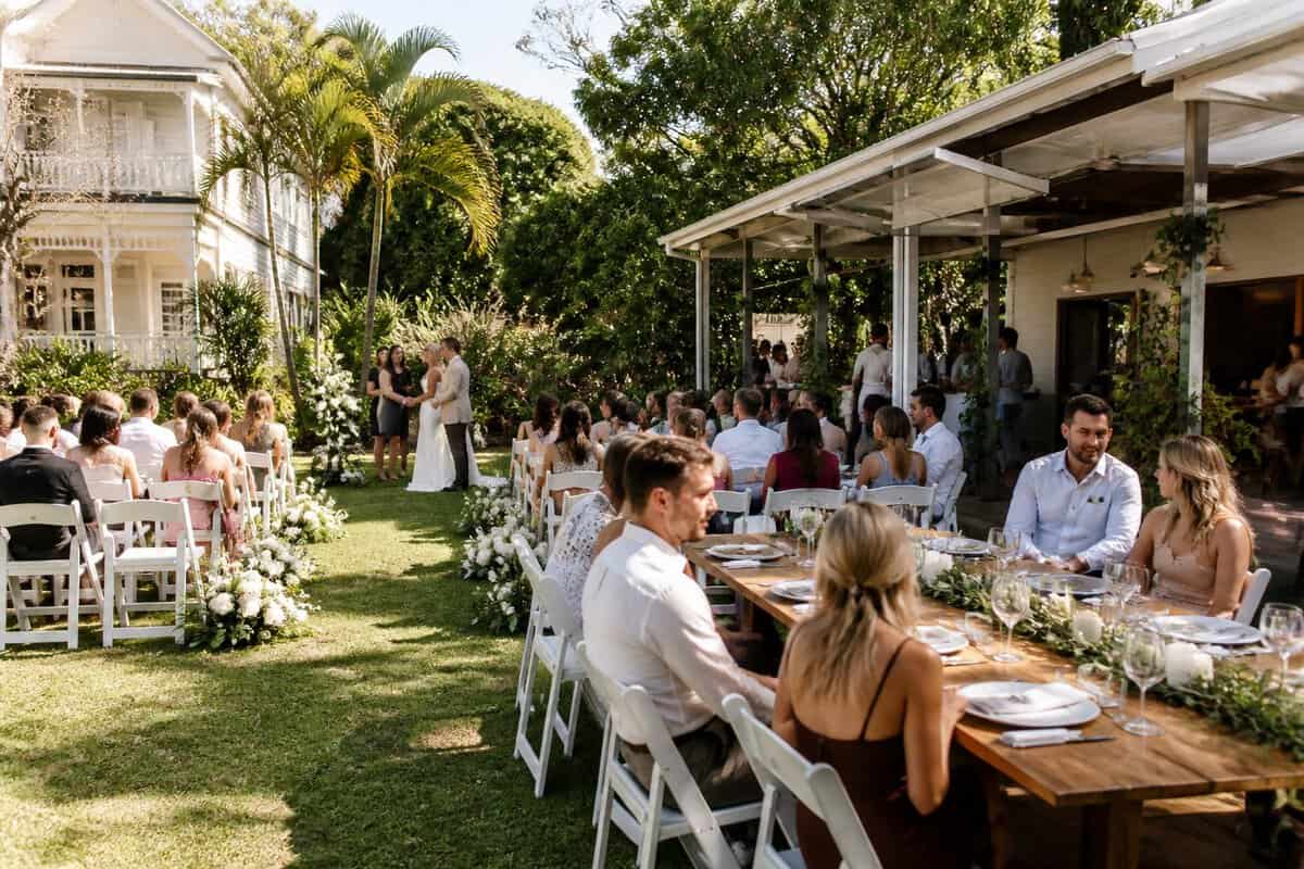 A couple and their guests celebrate at an elegant garden wedding venue with simple floral decorations and outdoor seating.