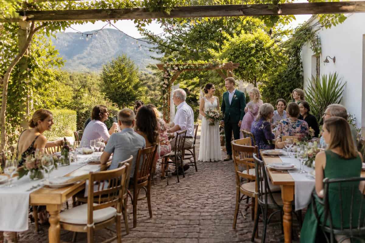 An intimate outdoor wedding with a small group of guests at simply decorated tables in a garden venue.