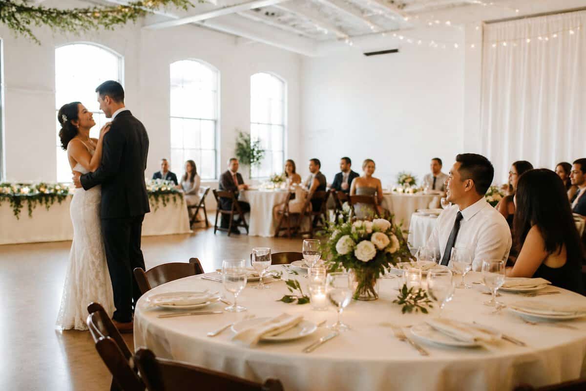 A warmly decorated, budget-friendly wedding reception venue with guests gathered around simple tables.