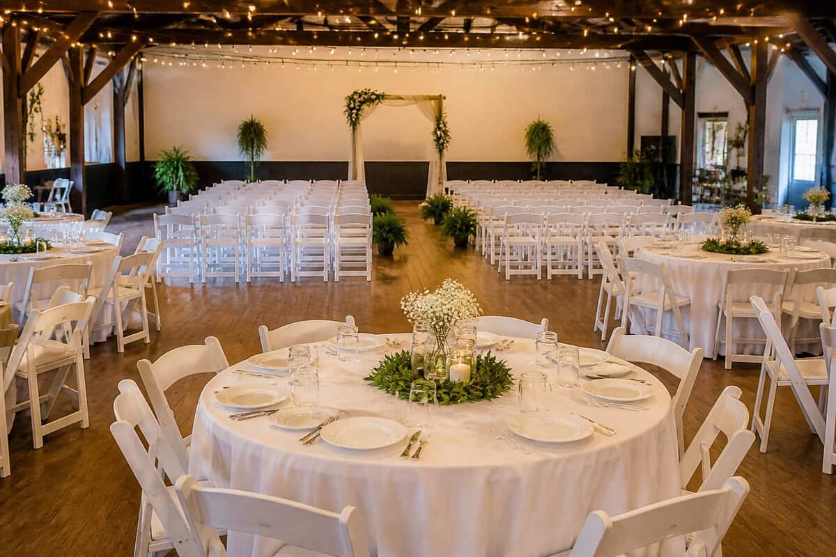 A modest wedding venue arranged with chairs, simple floral decor, reception tables, and warm string lights.