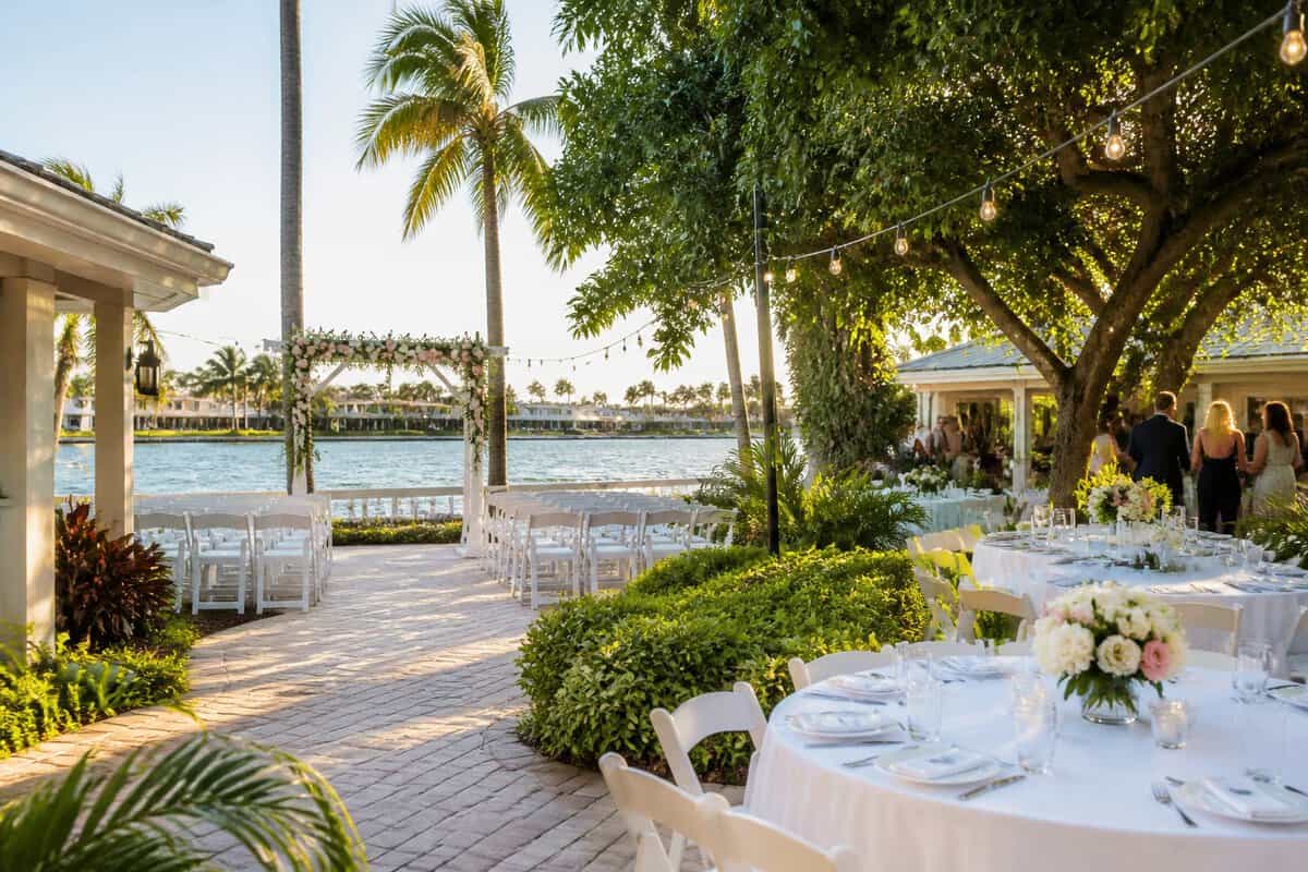 A couple and guests gather at an affordable waterfront wedding venue in Fort Lauderdale with palm trees, simple decorations, and outdoor tables.