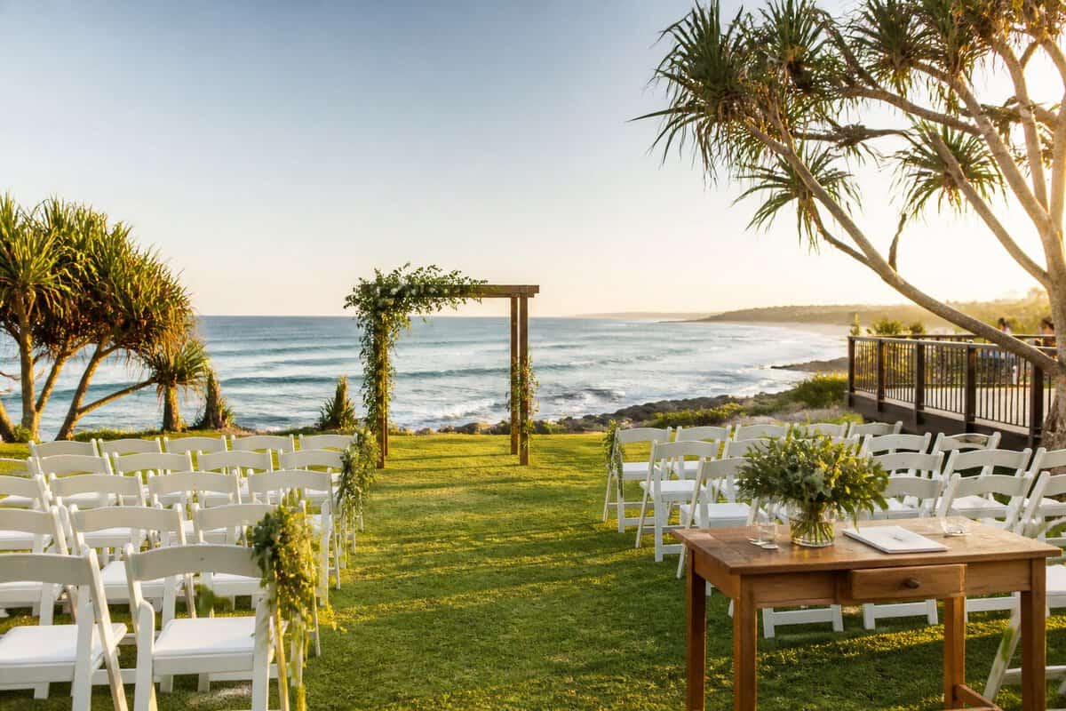 A simple outdoor wedding venue with white chairs, floral decorations, and a coastal landscape.