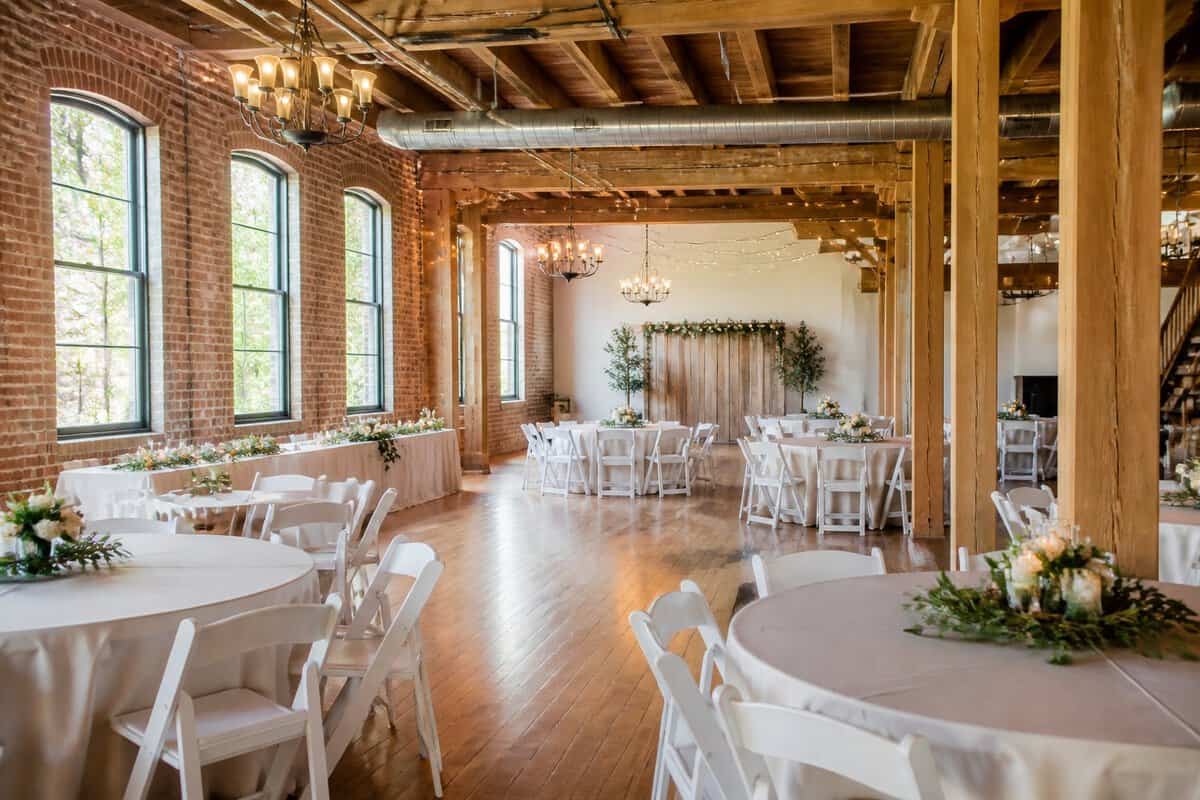 An affordable wedding venue with simple reception tables, greenery, exposed brick, and warm lighting.