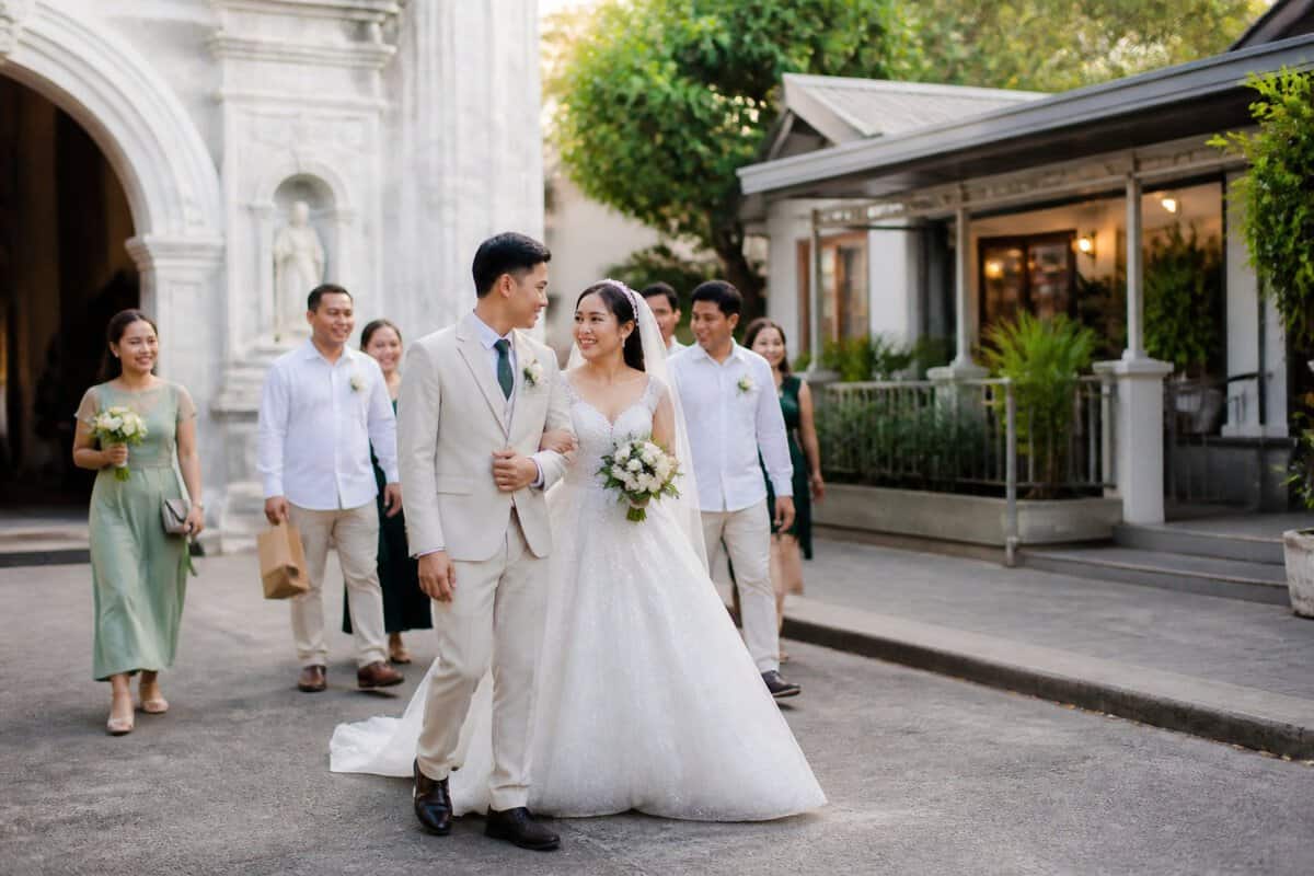 A newlywed couple and wedding guests walk from a church toward a nearby reception venue in Manila.
