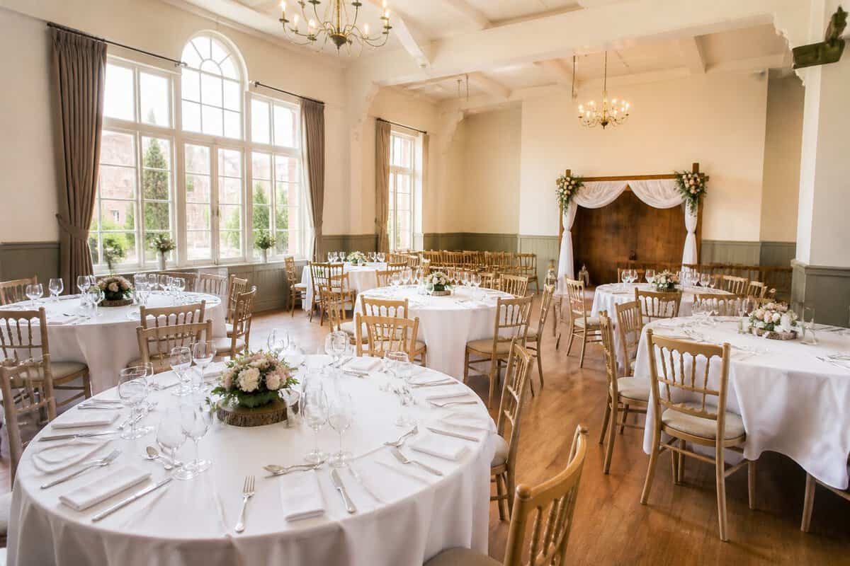 An elegant, modestly decorated wedding venue with round tables, floral arrangements, and large windows.