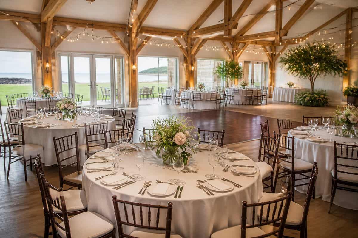 An elegant, modestly decorated wedding reception inside a charming Long Island venue with tables, flowers, warm lighting, and views of landscaped grounds.