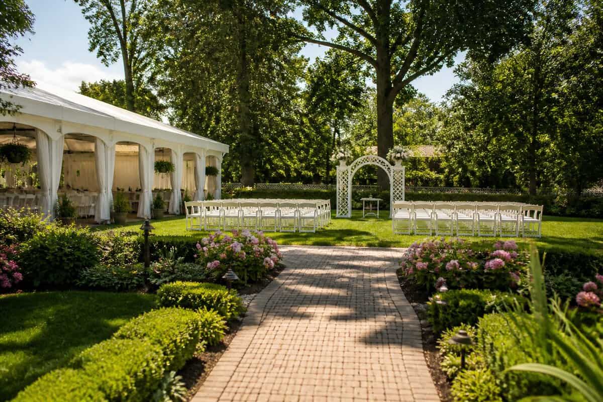 A garden wedding venue with flowers, trees, white chairs, and a simple ceremony arch.