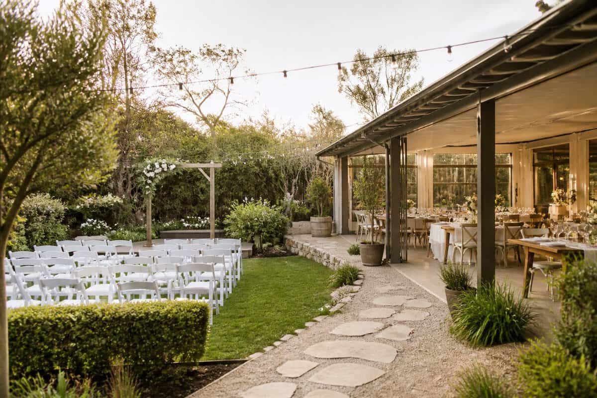 An elegant outdoor wedding venue with garden seating, a floral arch, and a covered reception area.