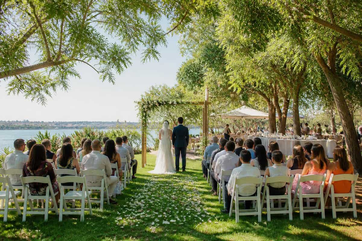A couple and guests at an elegant outdoor wedding venue with simple decorations and garden surroundings.