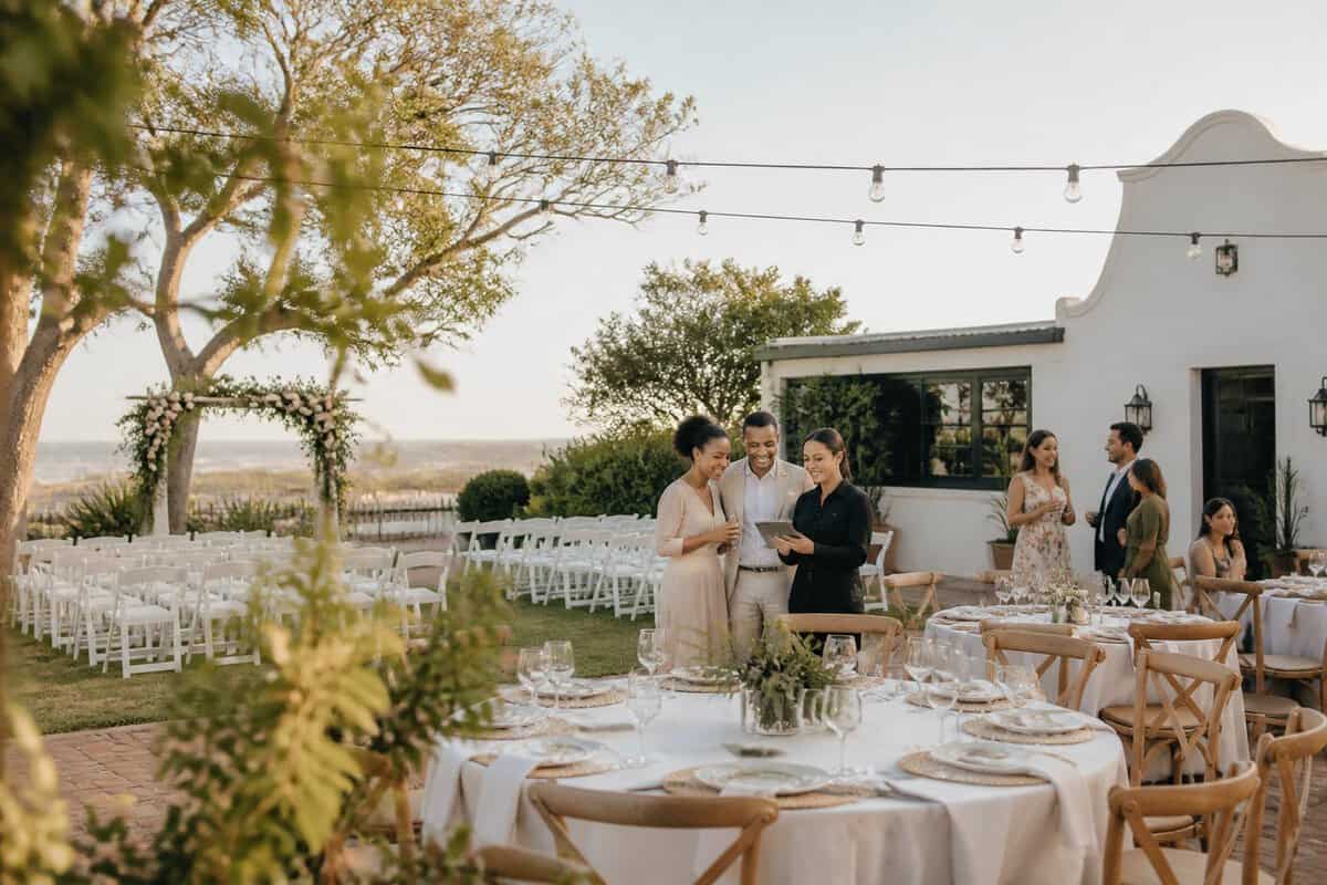 A modest outdoor wedding venue with simple decorations, reception tables, and guests gathered in a garden courtyard.