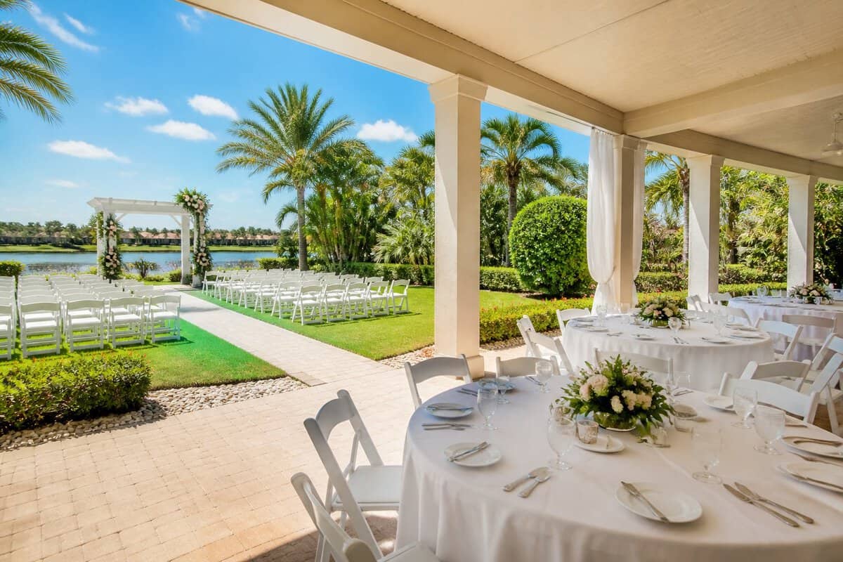 A modest outdoor wedding venue in Port St. Lucie with a white ceremony arbor, arranged chairs, tropical greenery, and a covered reception area.