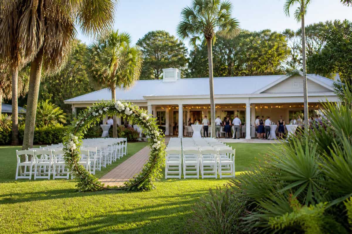 A charming coastal wedding venue with a simple outdoor ceremony setup surrounded by palms and tropical landscaping.