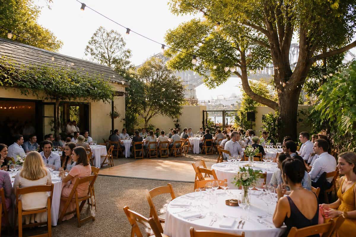 A modest garden wedding venue in Sydney with decorated tables, guests, greenery, and warm string lights.