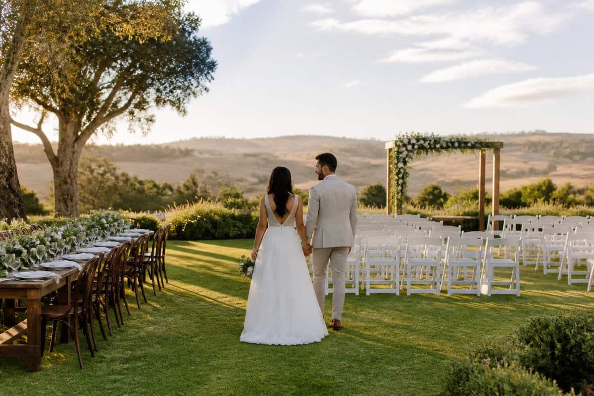 A couple stands in a scenic garden wedding venue with simple ceremony seating and floral decorations.