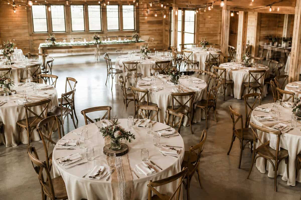 A warmly decorated wedding reception venue with simple elegant tables, seasonal flowers, and soft string lights.