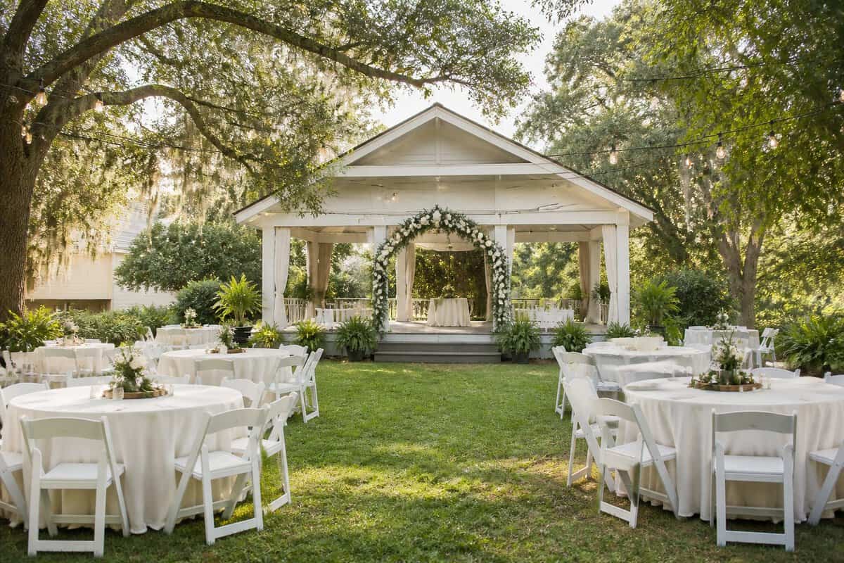 A modest outdoor wedding venue with a garden, oak trees, simple seating, and a decorated ceremony area.