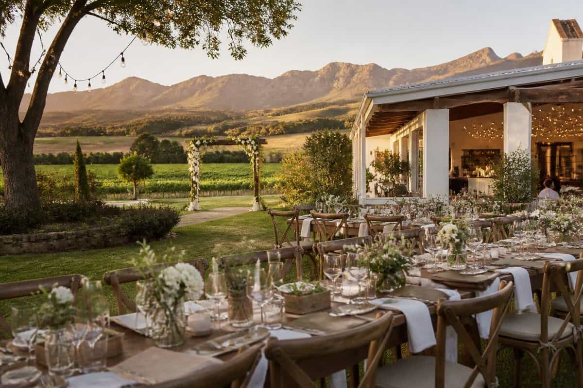 An elegant outdoor wedding venue with decorated tables, garden surroundings, and mountains in the distance.