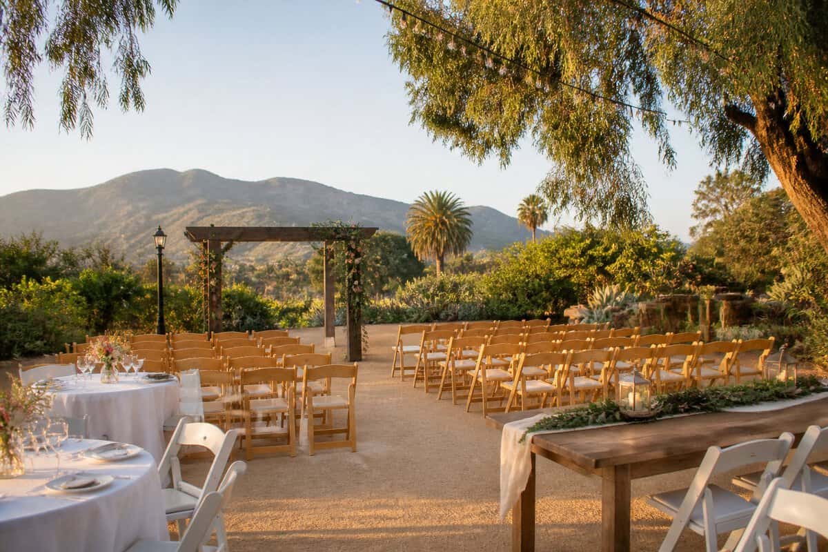 An intimate outdoor wedding setup with simple chairs, floral decorations, and string lights in a sunny garden venue.
