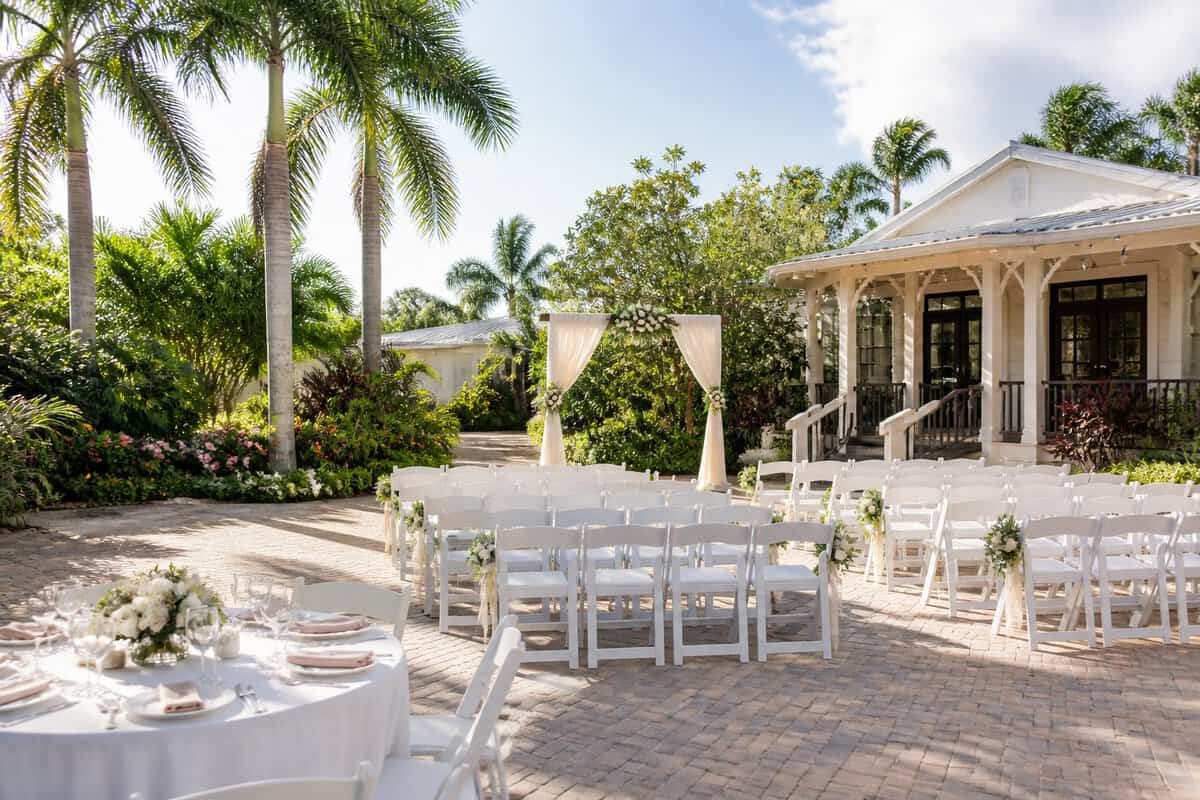 An affordable outdoor wedding venue with white chairs, a floral arch, tropical greenery, and a sunny South Florida setting.