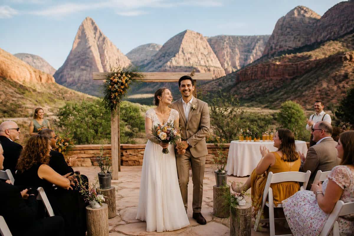Newlywed couple standing outside a simple wedding venue with Zion’s red cliffs in the background.