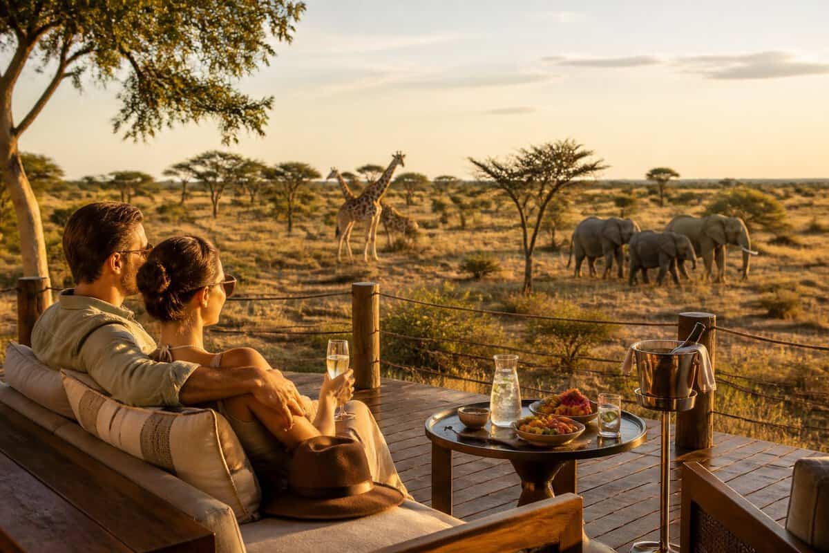 Newlywed couple relaxing on a safari lodge terrace overlooking a South African savanna with wildlife in the distance.