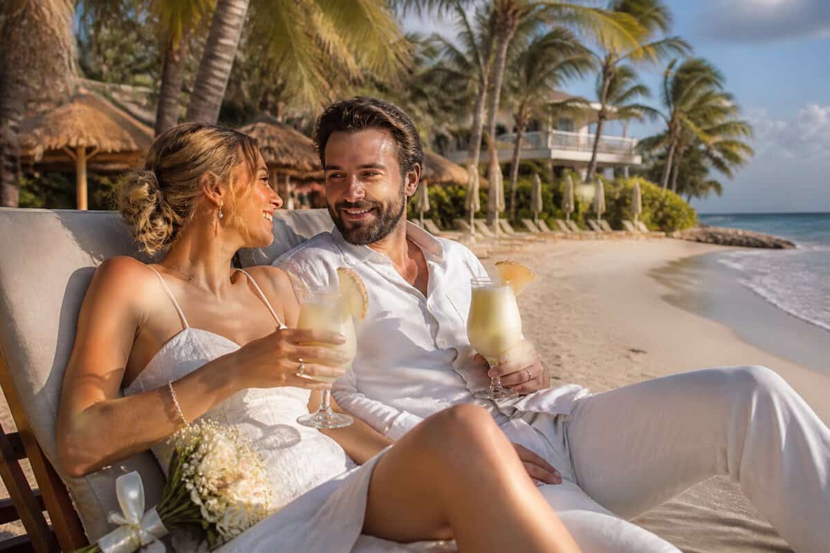 A newlywed couple shares a playful moment on a tropical beach outside an all-inclusive resort.