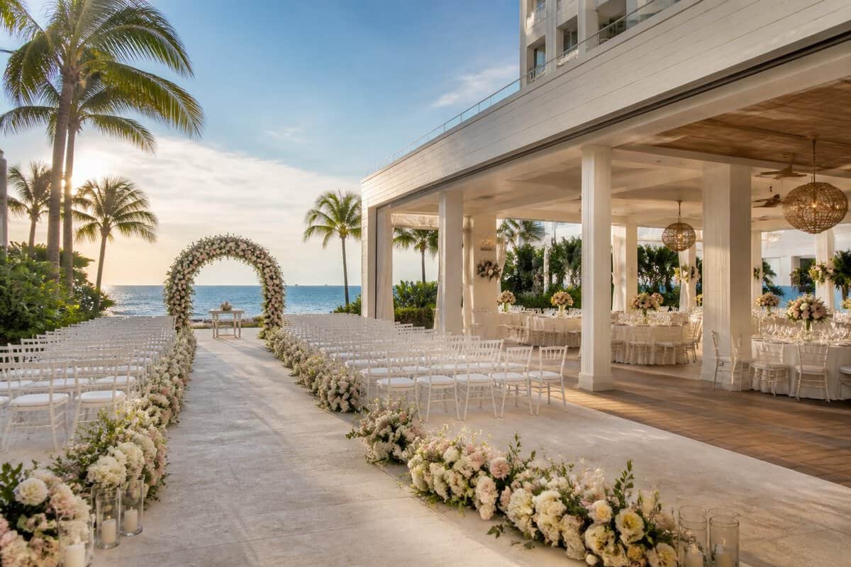 Elegant beachfront wedding venue in Fort Lauderdale with a floral ceremony arch, white chairs, tropical landscaping, and ocean views.