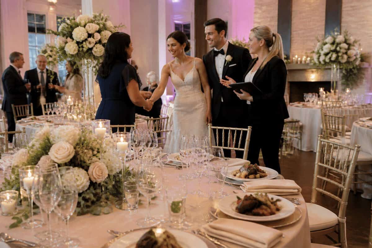 An elegant wedding reception with a decorated banquet table, floral centerpieces, and a couple greeting guests.
