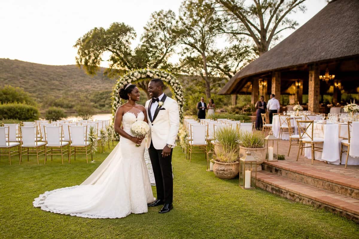 A bride and groom stand beside a decorated wedding ceremony arch at an elegant Zimbabwean outdoor venue.