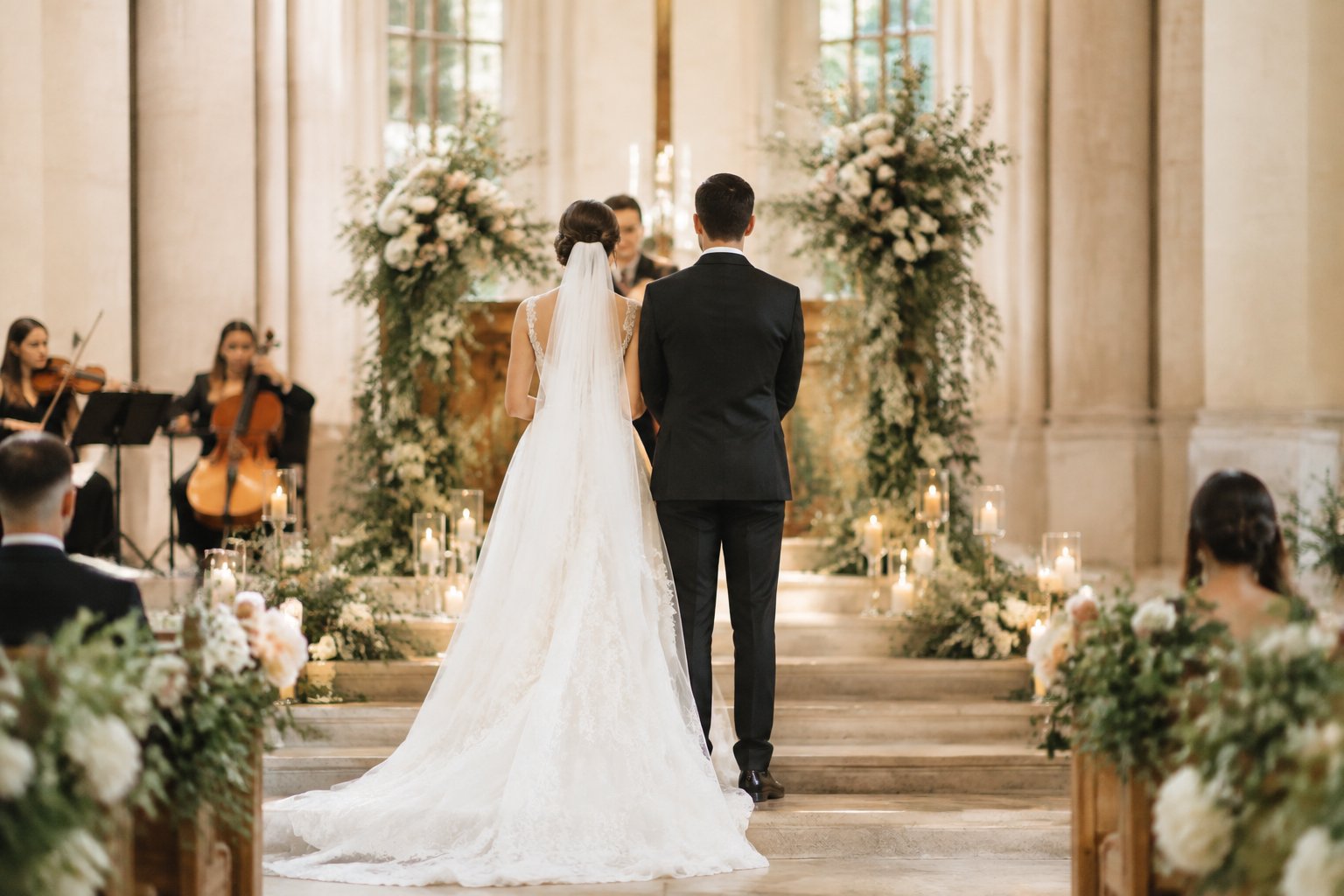 A bride and groom stand near a flower-decorated wedding altar while musicians play in the background.
