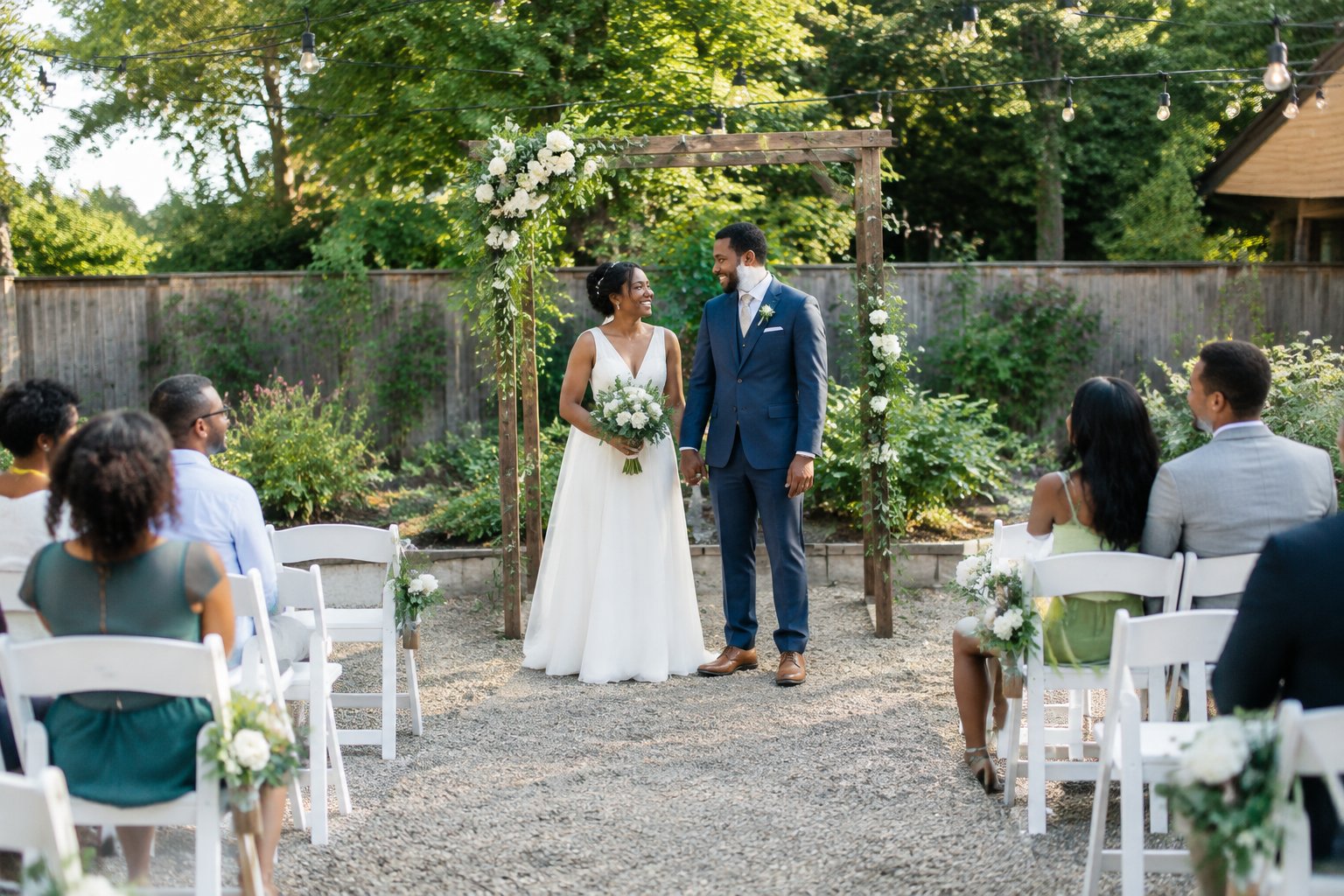 A couple celebrates an intimate outdoor wedding at a modest, beautifully decorated venue with family and friends.