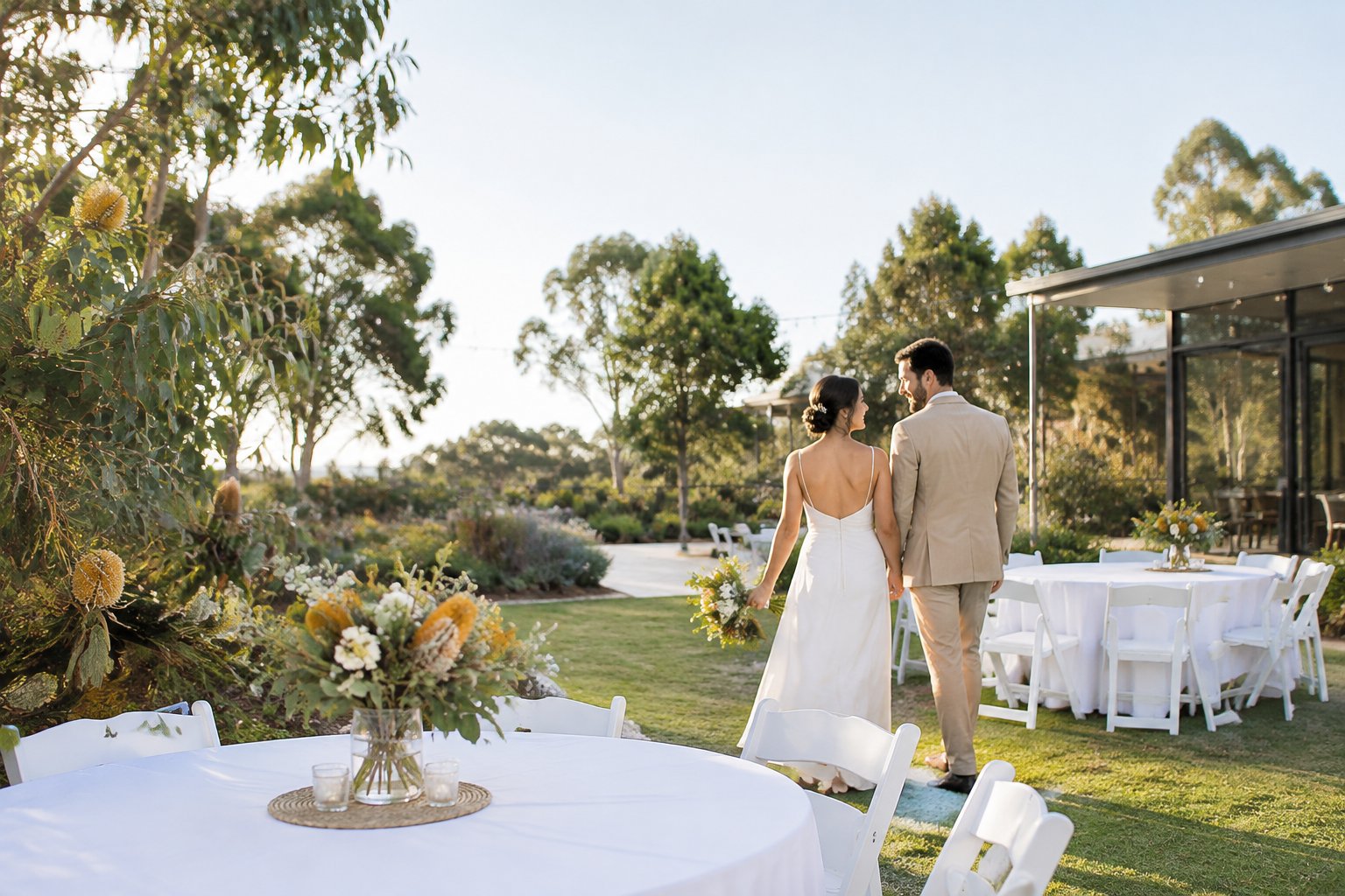 An intimate outdoor wedding reception with simple decorations, white chairs, and native Australian flowers.