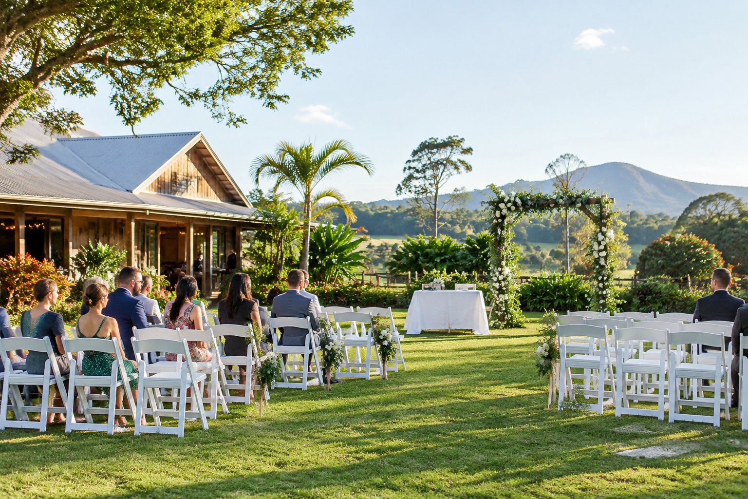 An affordable outdoor wedding venue with white chairs, a floral arch, and a garden beside a rustic event hall.