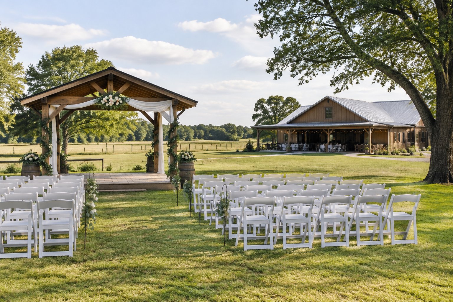 A modest outdoor wedding venue with white chairs, a rustic pavilion, and green fields.