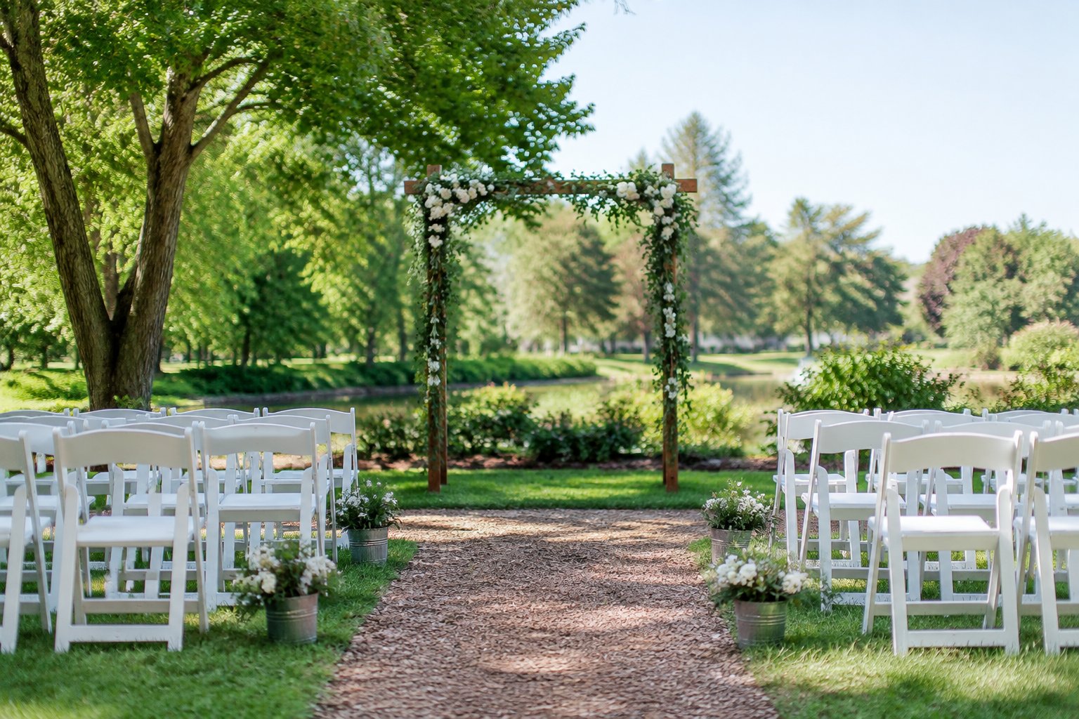 A simple outdoor wedding ceremony setup in a landscaped public garden with folding chairs and a flower-decorated arch.