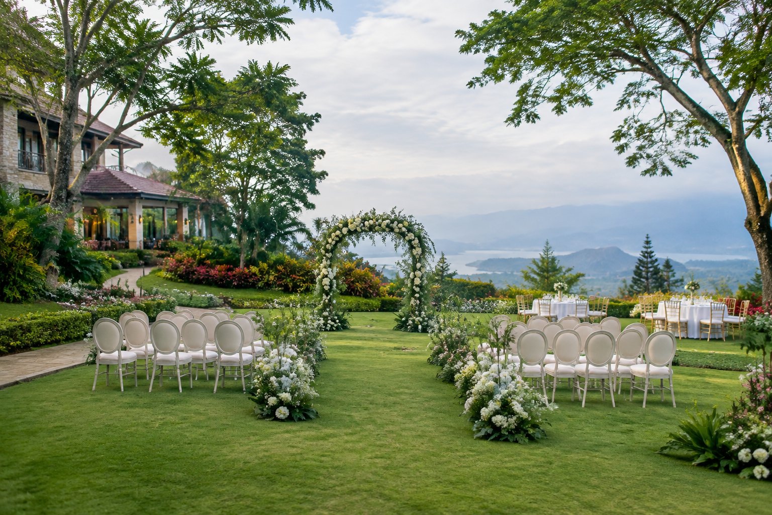 Elegant garden wedding venue in Tagaytay with a floral ceremony arch, white chairs, lush landscaping, and a distant mountain view.