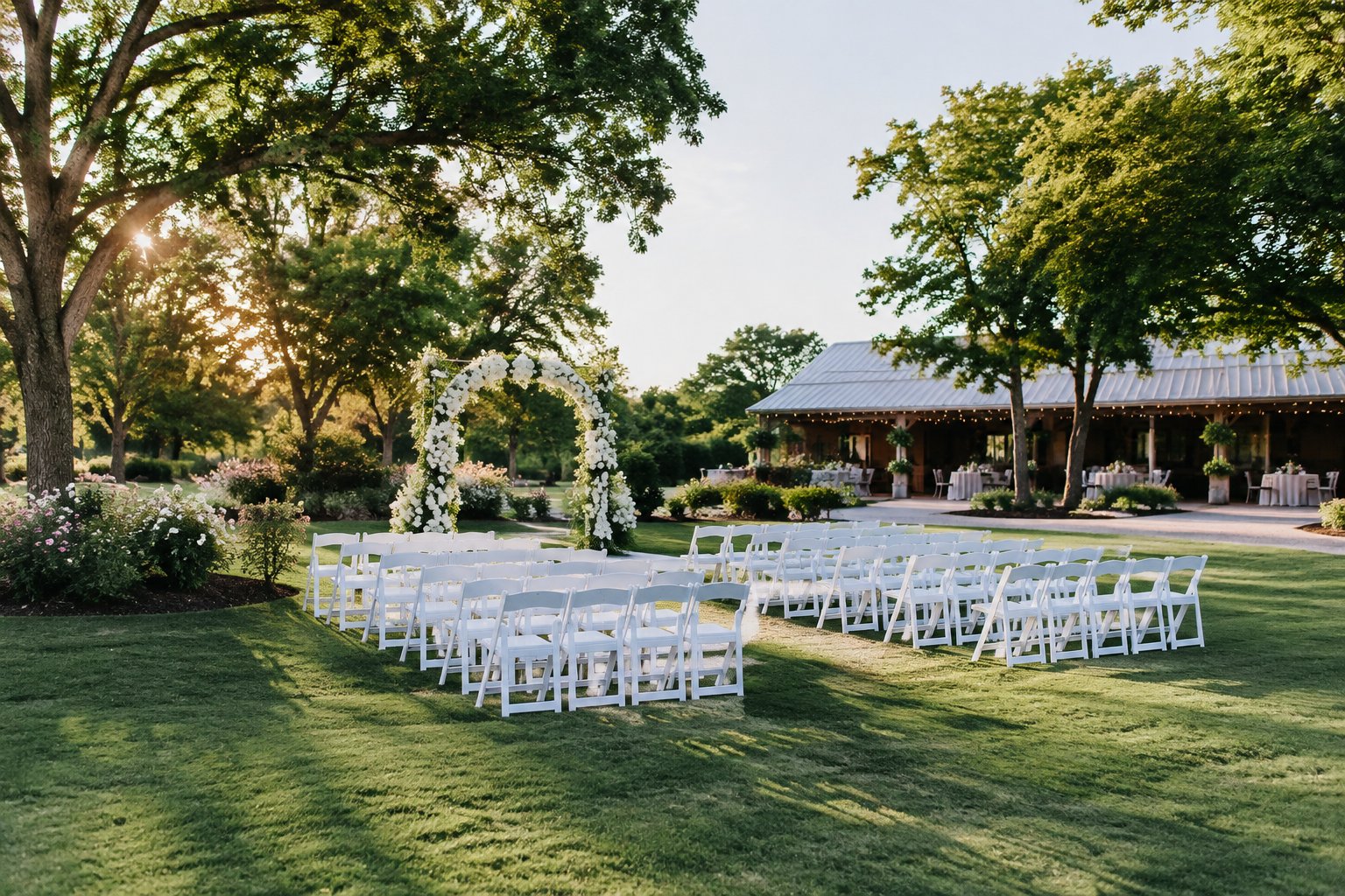 An elegant outdoor wedding ceremony setup in a lush garden with a floral arch and rows of white chairs.