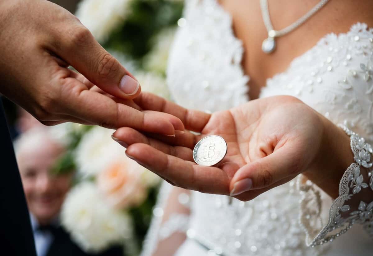 A hand places a sixpence in the bride's palm