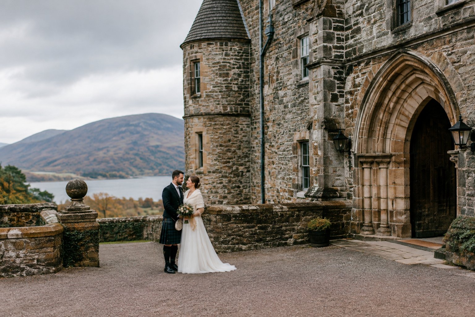 A couple stands together in the courtyard of a Scottish stone castle.